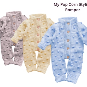 May include: Three knitted baby rompers in pastel shades: lavender, cream, and light blue. Each romper has a textured popcorn stitch and heart-shaped wooden buttons. The text "My Pop Corn Stylish Romper" is at the top.