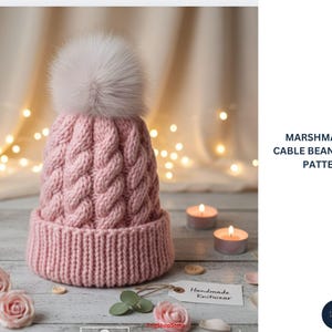 Puede incluir: Un gorro rosa tejido con trenzas con un pompón blanco esponjoso. El gorro tiene un borde acanalado y un diseño de trenzas texturizado. El texto "MARSHMALLOW CABLE BEANIE - KNIT PATTERN" es visible. La imagen también incluye velas encendidas y rosas.