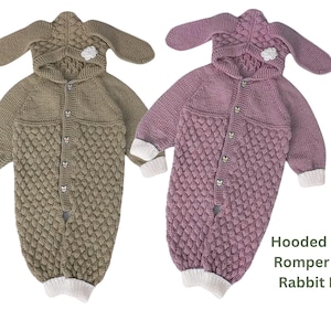 Peut inclure: Deux barboteuses pour bébés tricotées avec des capuches et des oreilles de lapin. L'une est vert olive, l'autre mauve. Les deux ont un motif texturé sur la moitié inférieure, des fermetures à boutons et des poignets blancs. Le texte dit "Barboteuse Bébé à Capuche avec Oreilles de Lapin."