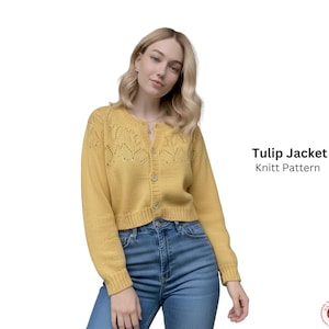 Op de afbeelding: Een vrouw draagt een mosterdgele, korte, gebreide cardigan met een knoopsluiting en een decoratief bladerpatroon. De tekst "Tulip Jacket Knitt Pattern" is zichtbaar. Ze draagt een blauwe spijkerbroek. Een stijlvol kledingstuk.