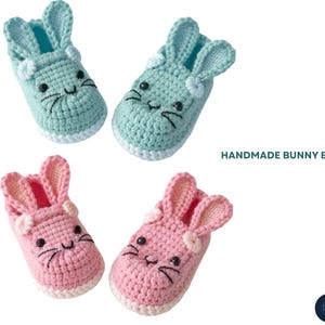 May include: Handmade bunny booties in two colors: light blue and pink. Each pair features a bunny face with embroidered details and a white sole. The text "HANDMADE BUNNY BOOTIES" is displayed on the right side.