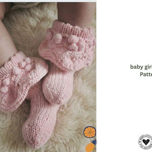 Puede incluir: Un par de calcetines rosas claros para bebé con un diseño de punto texturizado y detalles de pompón. Los calcetines se muestran sobre una superficie blanca y suave. Incluye el texto "baby girl socks, Pattern".