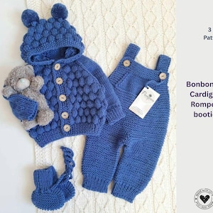 May include: A blue knitted baby set comprising a hooded cardigan with wooden buttons, dungarees, and booties. The set has a textured pattern and includes a small grey teddy bear. The image text reads "Bonbon Candy Cardigan and Romper with booties set."