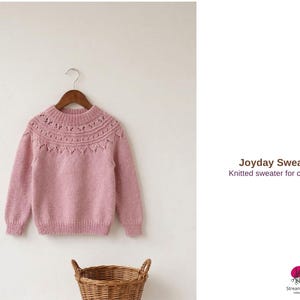 May include: A light pink knitted sweater for children, hanging on a wooden hanger. The sweater features a detailed neckline design and long sleeves. The text "Joyday Sweater" and "Knitted sweater for children" are visible.