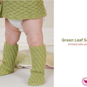 Puede incluir: Calcetines de tubo tejidos de color verde claro con un patrón de hojas. Los calcetines son hasta la rodilla y se muestran en un bebé. El tejido es texturizado.
