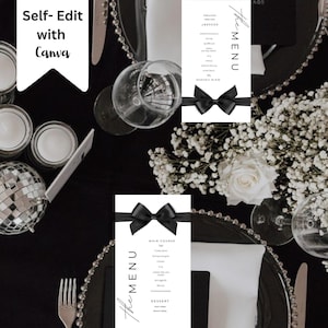 May include: Two white cards with black ribbon bows and the text "The Menu" printed in black cursive. The cards are on a black table setting with white flowers and a silver charger plate.