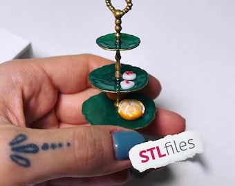 Puede incluir: Miniatura de bandeja de tres niveles con platos verdes y un asa dorada. La bandeja contiene pequeños postres, incluyendo dos golosinas blancas en forma de corazón con puntos rojos y una pequeña fruta naranja. El texto "STL files" es visible.
