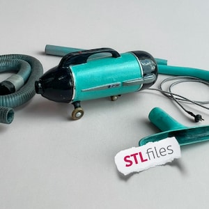 以下が含まれることがあります： ハンドル、車輪、シルバーのアクセントが付いた、ターコイズと黒のヴィンテージスタイルのヘアドライヤー。灰色のホースとアタッチメントが近くにあります。画像には「STLfiles」と書かれたタグが含まれています。