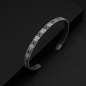 May include: A silver bangle bracelet with a decorative pattern of black circles and swirls.