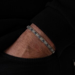 May include: A silver bracelet with a delicate design featuring small blue gemstones. The bracelet is worn on a person's wrist.
