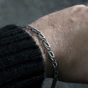 May include: A silver chain bracelet with a curb link design. The bracelet is worn on a person's wrist.