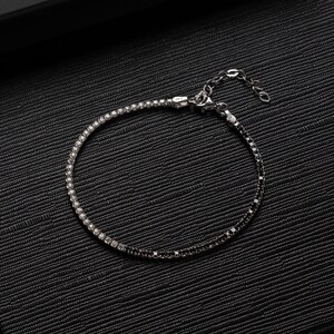May include: A silver bracelet with a black and white diamond design. The bracelet has a clasp closure.