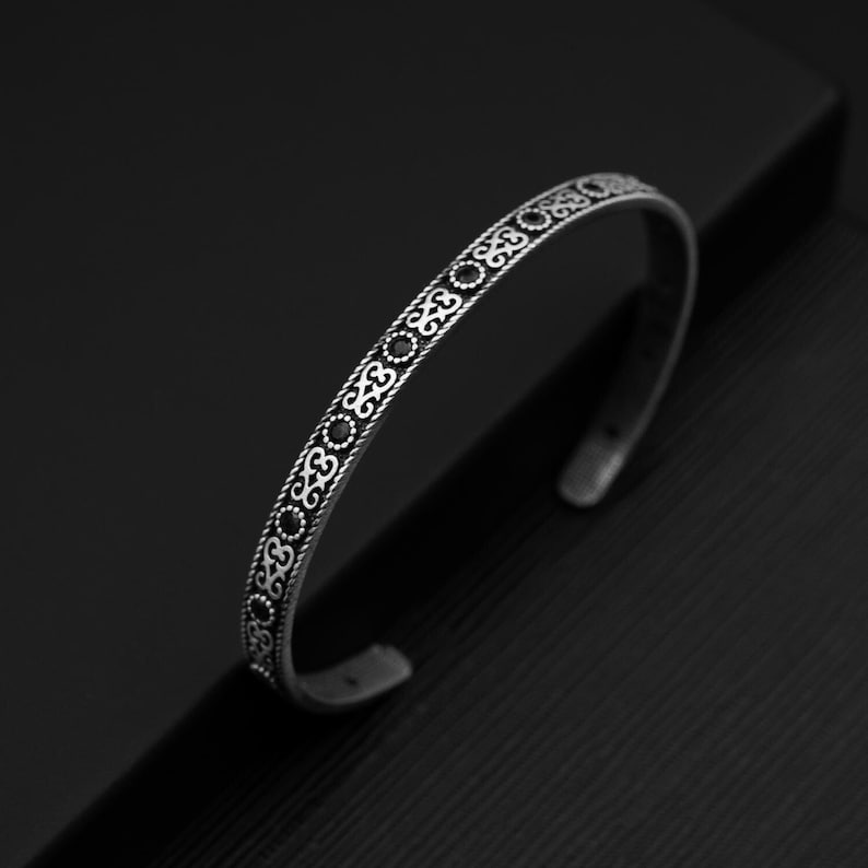 May include: A silver bangle bracelet with a decorative pattern of black circles and swirls.