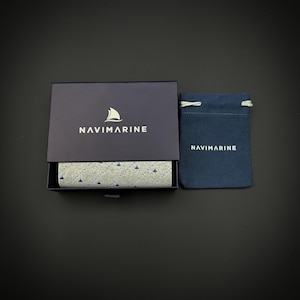 May include: A black box with the word "NAVIMARINE" printed on the top. The box is open and shows a patterned lining with the same logo. A small blue drawstring bag with the same logo is next to the box.