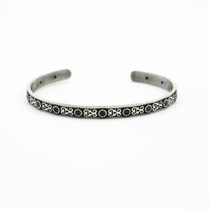 May include: A silver bangle bracelet with a black and silver patterned design.
