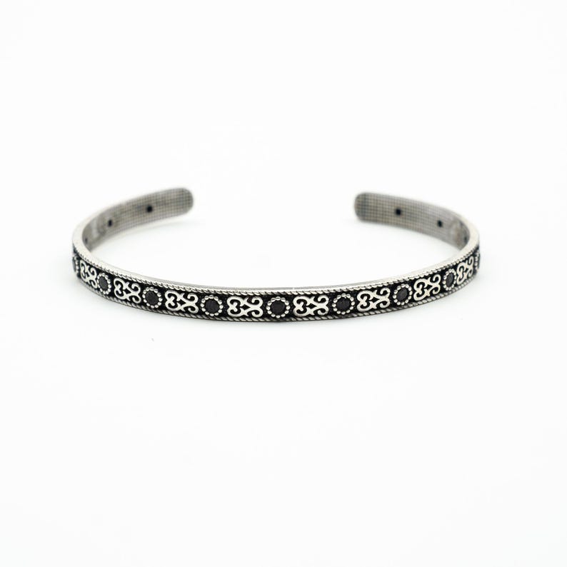 May include: A silver bangle bracelet with a black and silver patterned design.