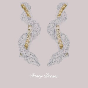 May include: A pair of elegant, abstract earrings. The earrings feature a silver-colored, intertwined design, accented with yellow-gold and clear gemstones. The earrings are set against a soft pink background, with the text "Fancy Dream" in cursive.