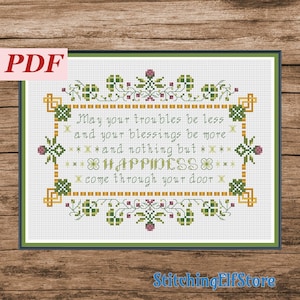 May include: Cross stitch pattern featuring a green and gold frame with a floral design. The text inside the frame reads: "May your troubles be less and your blessings be more and nothing but happiness come through your door."