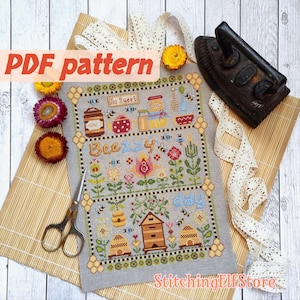 May include: A PDF pattern for cross-stitch embroidery featuring a bee-themed design with the text "Bee-zy as a bee" and "Stitching Elf Store". The design includes bees, honeycombs, flowers, and jars of honey.