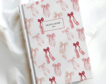 Puede incluir: Un cuaderno blanco con un patrón de lazos rosas y rojos. La portada tiene el texto "Olivia Rose notes" impreso.
