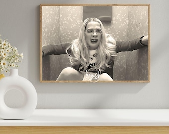 May include: A framed black and white photograph depicting a person with long wavy hair, wearing a long-sleeved top, positioned in a small space with floral wallpaper. The person has an expressive facial expression with an open mouth.
