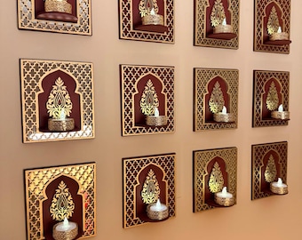May include: A collection of eleven square wall-mounted candle holders featuring a dark maroon background with gold-colored intricate lattice patterns and a central arch design. Each holder includes a small shelf supporting a lit tea light candle.