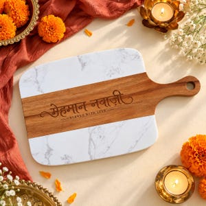 May include: A rectangular serving board featuring a white marble finish on the top and bottom sections with a central horizontal strip of natural brown wood. The wood section is engraved with the Hindi text "मेहमान नवाज़ी" and "SERVED WITH LOVE".