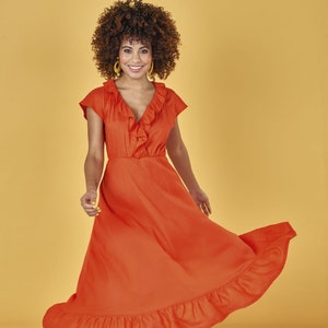 May include: A woman wearing a bright orange dress with a ruffled neckline and a ruffled hem. She is wearing yellow sandals and has curly brown hair.