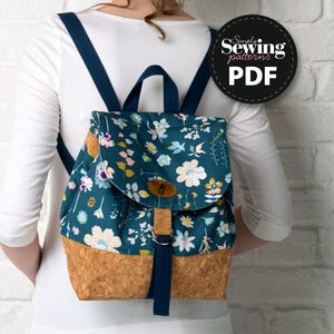 Peut inclure: Un sac à dos bleu et blanc à fleurs avec un fond en liège et une sangle bleu marine. Le sac à dos a un rabat avec une boucle en cuir et un charme d'abeille. Le texte "Simply Sewing patterns PDF" est sur un cercle noir.