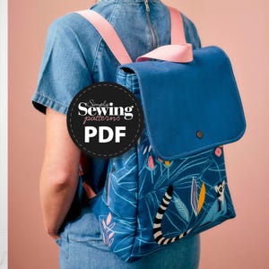 Op de afbeelding: Een blauwe rugzak met een roze band en een klep sluiting. De rugzak heeft een blauwe en witte gepatroneerde stof met een lemur ontwerp. De tekst "Simply Sewing patterns PDF" staat op een zwarte cirkel.