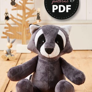 May include: A gray plush raccoon stuffed animal sitting on a wooden floor. The raccoon has black eyes, a white nose, and black and white markings around its eyes. The stuffed animal is wearing a black and white striped tail. The image includes the text "Simply Sewing patterns PDF".