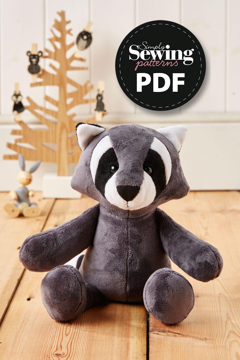May include: A gray plush raccoon stuffed animal sitting on a wooden floor. The raccoon has black eyes, a white nose, and black and white markings around its eyes. The stuffed animal is wearing a black and white striped tail. The image includes the text "Simply Sewing patterns PDF".