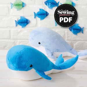 May include: Two whale plush toys, one blue and one light blue, with white bellies and black eyes. The whales are on a white surface with a white brick wall in the background. The image also includes a black circle with the text "Simply Sewing Patterns PDF".