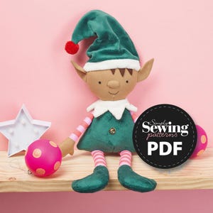 May include: A green and pink elf doll with a red pom-pom hat, sitting on a wooden shelf with a pink and gold ornament and a white star. The doll is wearing a green and white striped shirt and pants. The image includes the text "Simply Sewing patterns PDF".