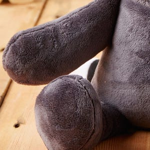 May include: A plush raccoon toy with a gray and white striped tail. The toy is sitting on a wooden surface.