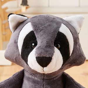 May include: A plush raccoon toy with a gray and white face and black eyes. The toy is made of soft, cuddly fabric and is perfect for cuddling.
