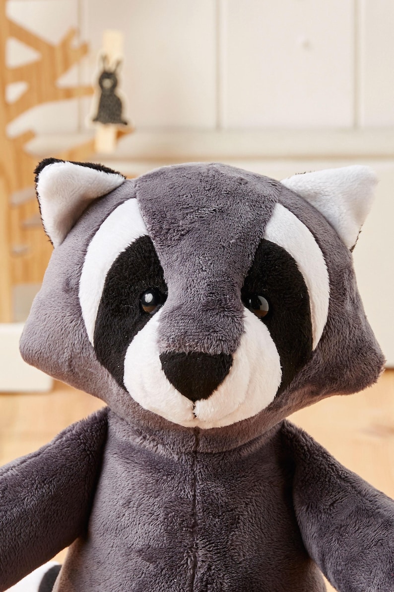 May include: A plush raccoon toy with a gray and white face and black eyes. The toy is made of soft, cuddly fabric and is perfect for cuddling.