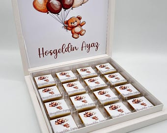 May include: A white box with a lid containing 16 individually wrapped chocolates. The lid has a picture of a teddy bear holding balloons and the text "Hosgeldin Ayaz".