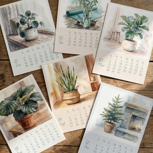 Może przedstawiać: Kolekcja kalendarzy w stylu akwarelowym z ilustracjami botanicznymi. Każda strona kalendarza przedstawia inną roślinę domową, taką jak figowiec lirolistny lub wężownica, z miesiącem i dniami. Kalendarze są ułożone na drewnianej powierzchni.