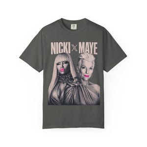 Może przedstawiać: Ciemnoszary t-shirt z krótkim rękawem z nadrukiem graficznym przedstawiającym dwie osoby oraz napisem NICKI X MAYE powyżej. Obie postacie są w czarno-białym stylu fotograficznym, z jaskraworóżowymi ustami jako jedynym kolorowym akcentem.
