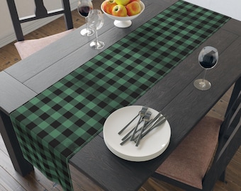 Könnte beinhalten: Ein grüner und schwarzer karierter Tischläufer auf einem dunklen Holztisch mit einer Schüssel Äpfel, zwei Weingläsern und einem Besteck auf einem weißen Teller.