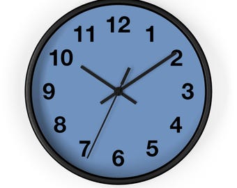 May include: Round wall clock with a black frame, black hands, and black numerals on a light blue face. The clock face displays the numbers 1 through 12. The hands indicate the time is approximately 10:10.