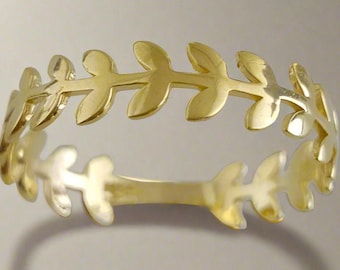 May include: A gold-colored ring featuring a repeating leaf design. The leaves are evenly spaced around the band, creating a delicate and nature-inspired aesthetic. The ring is shown against a neutral background.