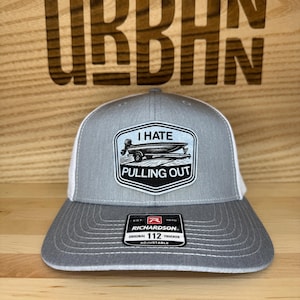 May include: Gray and white trucker hat with a patch that reads "I Hate Pulling Out" with a boat graphic. The hat is adjustable and has a Richardson 112 tag.