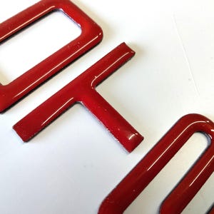 Könnte beinhalten: Nahaufnahme von roten Plastikbuchstaben, die "DIY" buchstabieren. Die Buchstaben sind erhaben und haben eine glänzende Oberfläche.