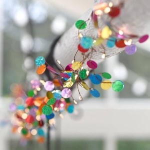 Puede incluir: Una guirnalda de luces decorativa con un fino cable de cobre adornado con numerosos discos circulares peque&ntilde;os y multicolores en tonos rojo, azul, verde, amarillo y morado, creando un despliegue de luz vibrante y reflectante.