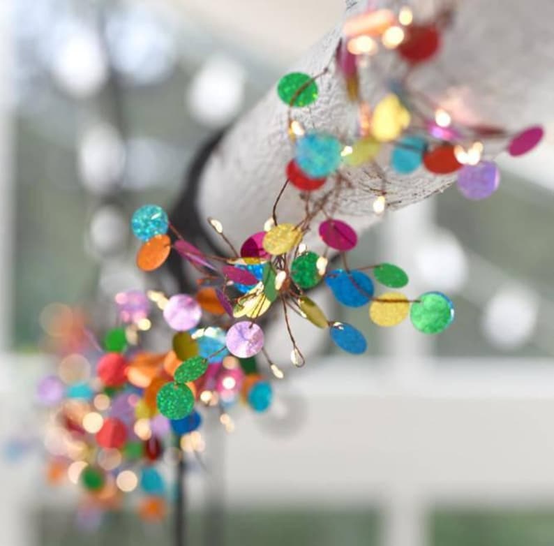 Puede incluir: Una guirnalda de luces decorativa con un fino cable de cobre adornado con numerosos discos circulares peque&ntilde;os y multicolores en tonos rojo, azul, verde, amarillo y morado, creando un despliegue de luz vibrante y reflectante.