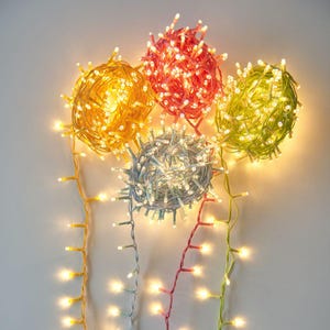 以下が含まれることがあります： 4本のフェアリーライトが、それぞれボール状に巻かれています。ライトは白で、ワイヤーの色は黄色、赤、緑、青です。