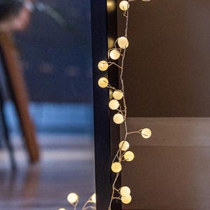 May include: String of warm white globe lights. The lights are strung on a thin, silver wire and are evenly spaced. The background is a dark brown and black.