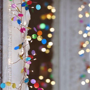 Puede incluir: Una guirnalda de luces decorativa con un fino cable de cobre entrelazado con peque&ntilde;os discos circulares brillantes de colores rojo, azul, verde, amarillo, morado y naranja, acentuada con diminutas luces LED de color blanco c&aacute;lido.